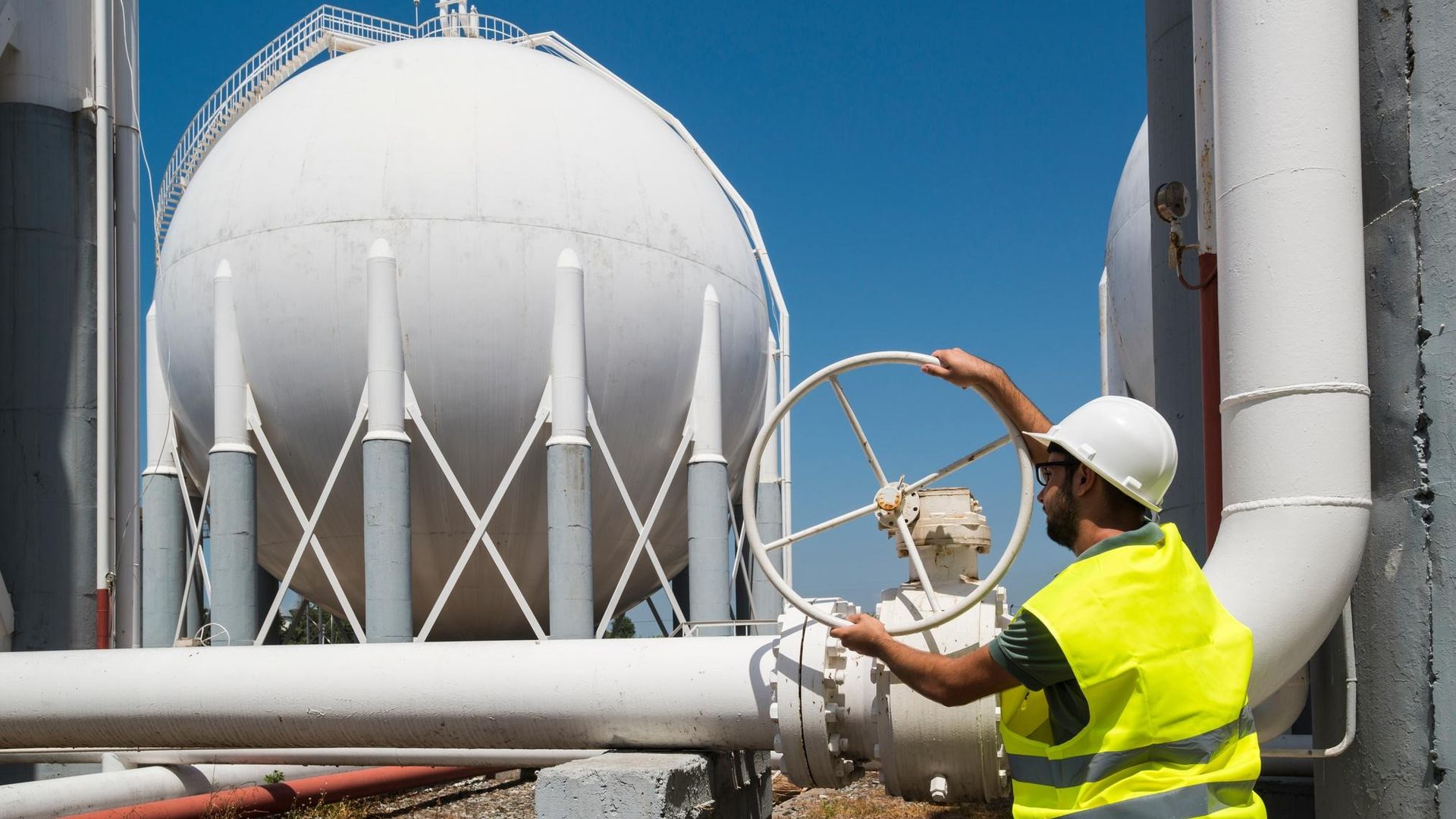 Engineer operating a valve beside gas storage spheres